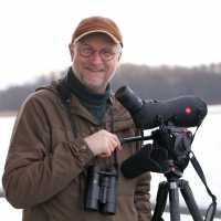 prof. Piotr Tryjanowski podczas obserwacji ptaków, w tle jezioro oraz drzewa